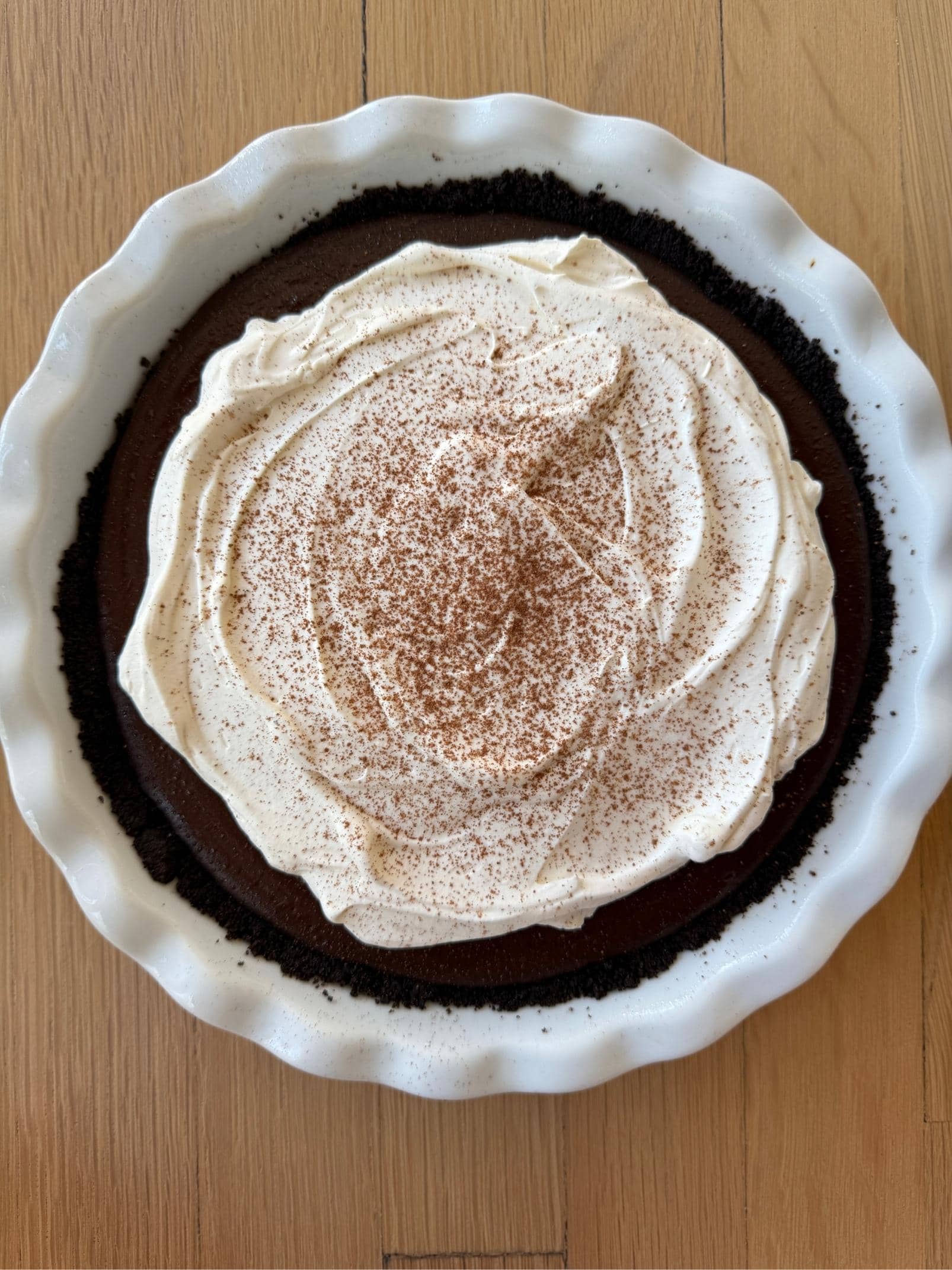 iPhone photo of chocolate cream pie in a white ceramic dish on a wood countertop