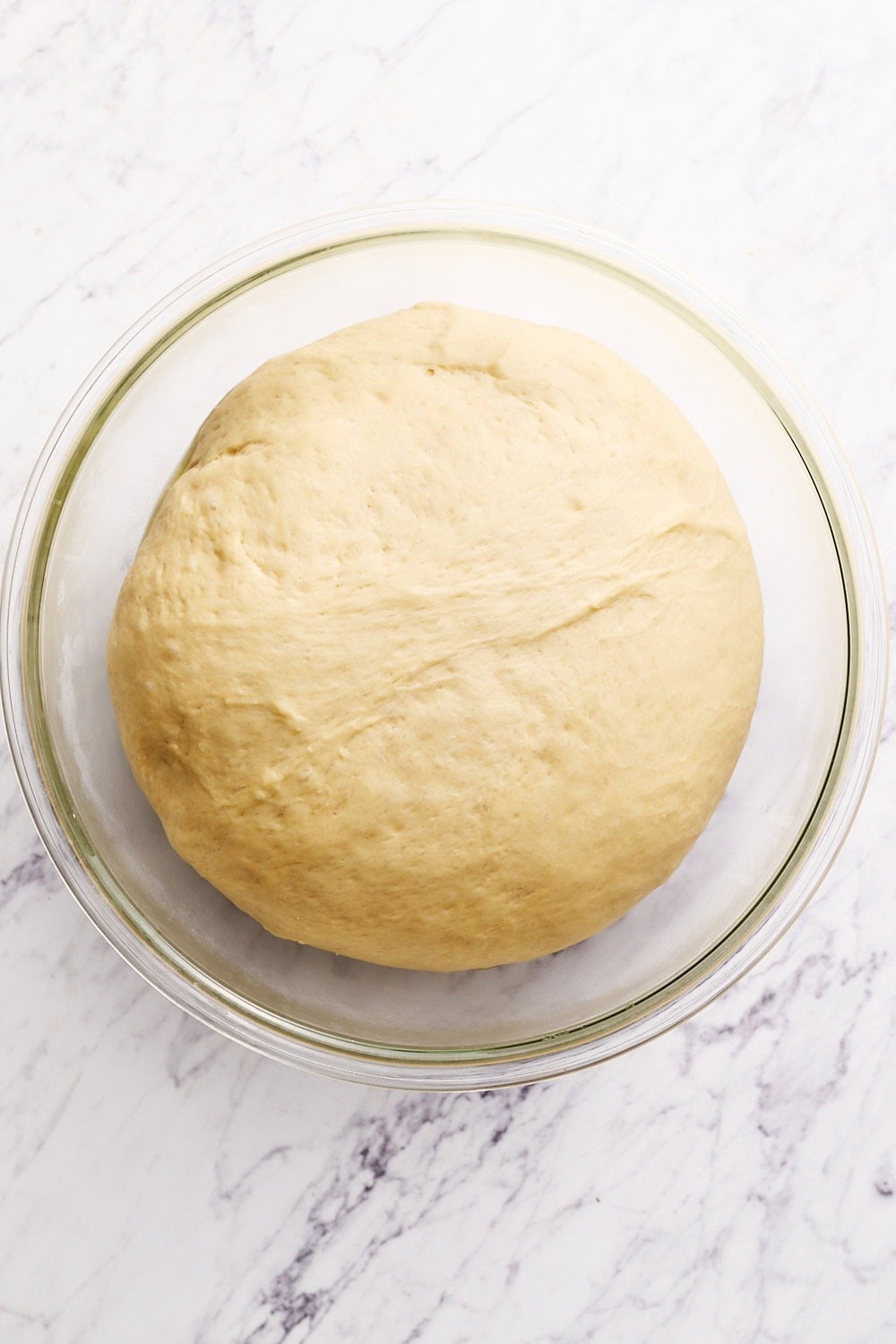 cinnamon roll dough in a glass bowl on a marble surface after rising