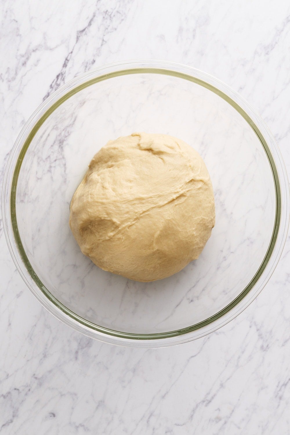 cinnamon roll dough in a glass bowl on a marble surface before rising