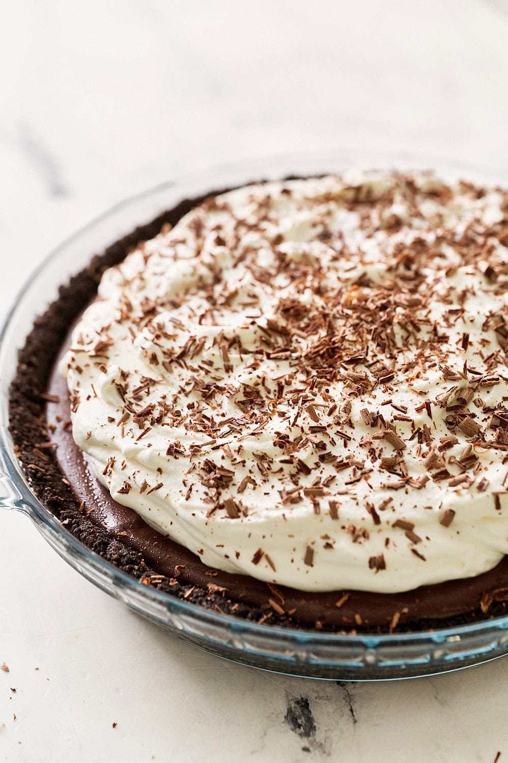 three quarter angle shot of the chocolate cream pie topped with whipped cream and chocolate shavings on a marble counter