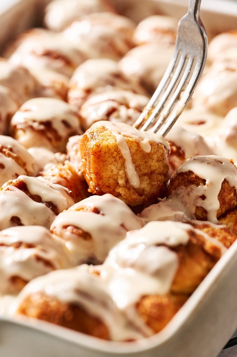 fork lifting up a cinnamon bun bites from the pan to reveal the soft, gooey interior