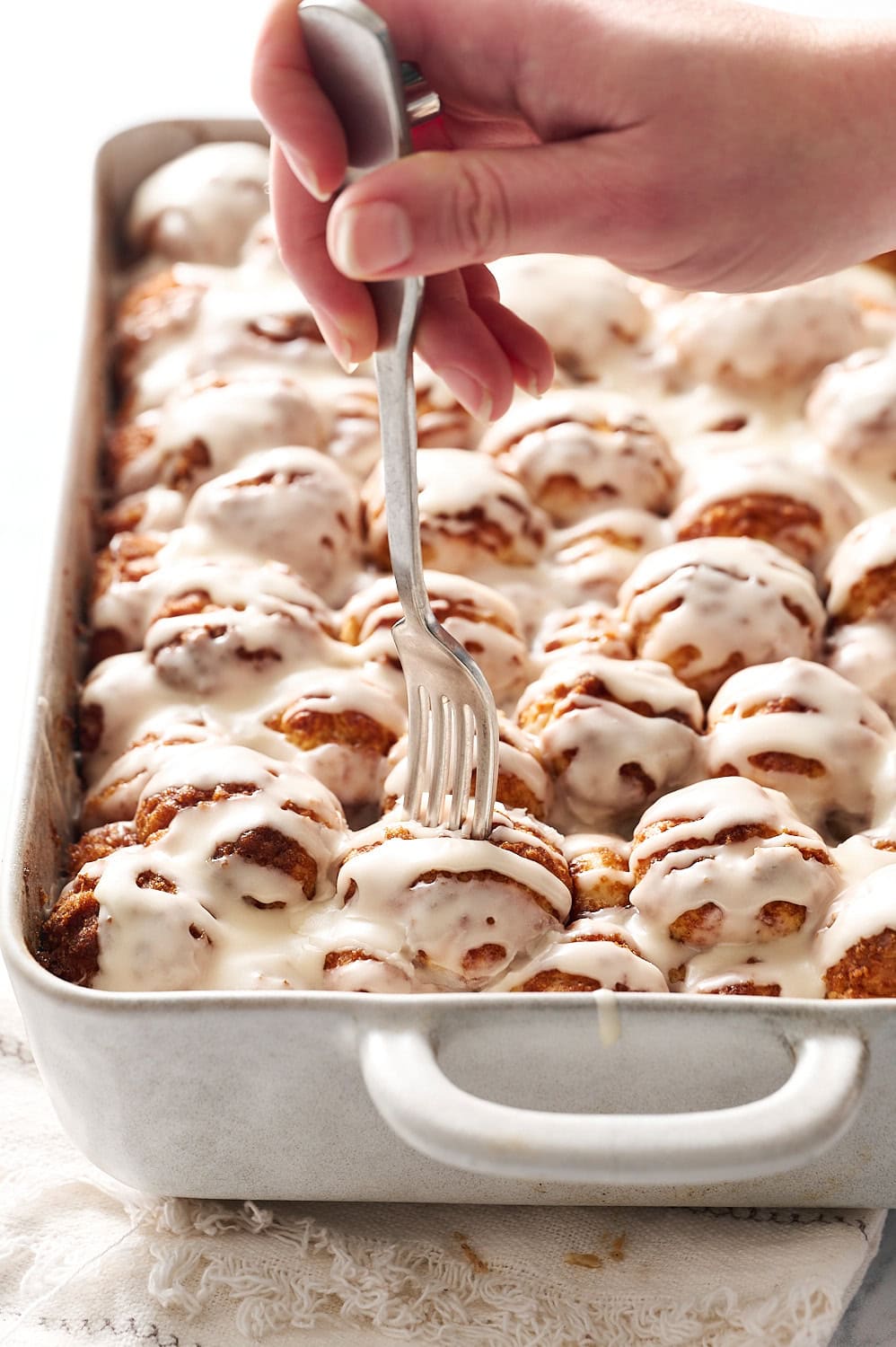 a hand holding a fork, pressing into one of the cinnamon bun bites in the pan