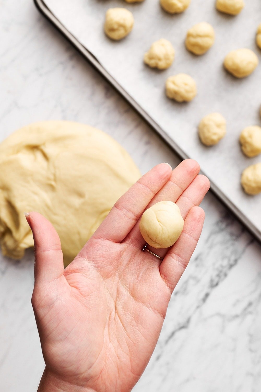 hand holding a ball of dough with tray filled with dough balls underneath