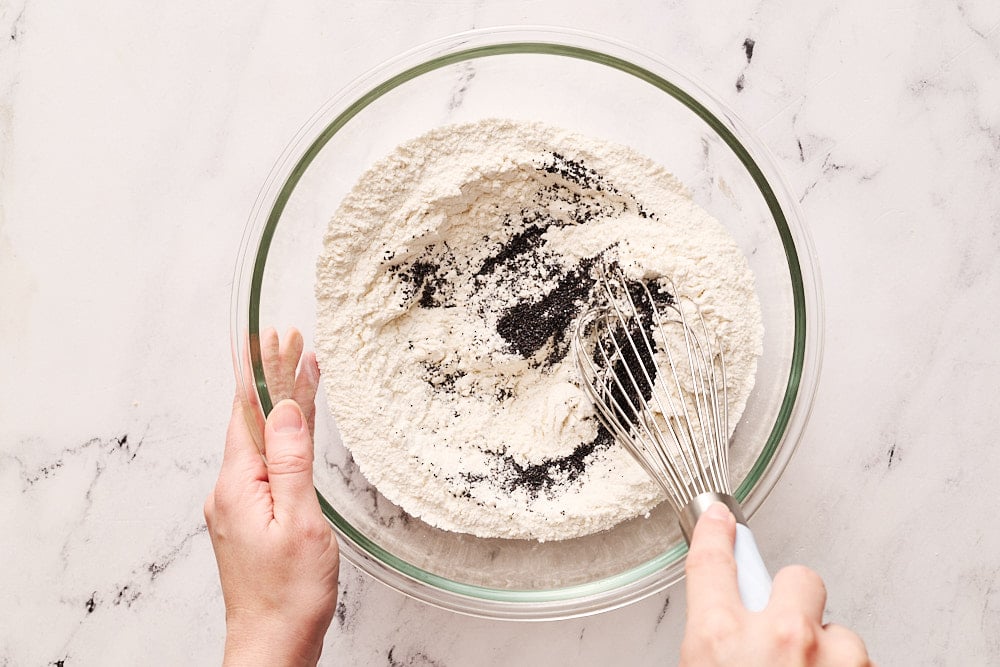 mixing dry ingredients for lemon poppyseed muffins in a glass bowl with a whisk