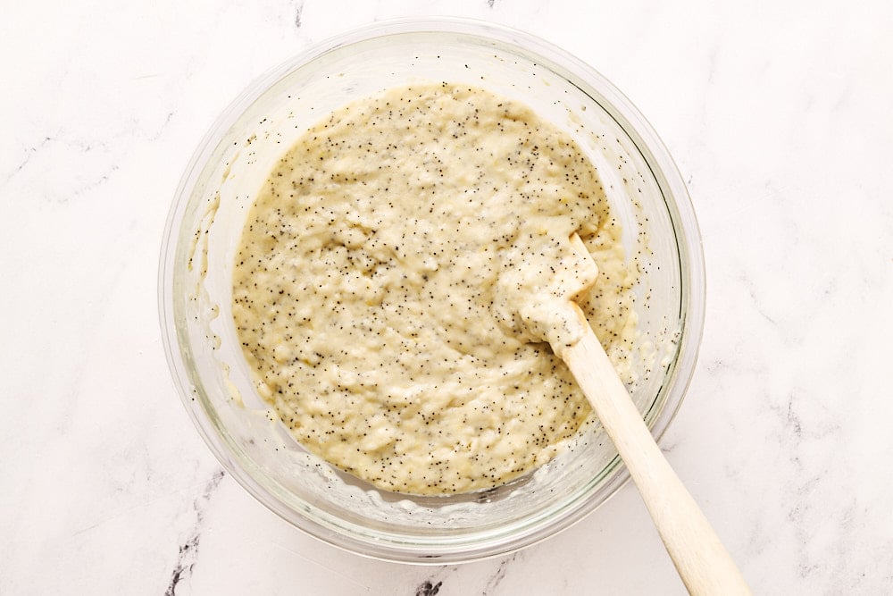 lemon poppyseed muffin batter in glass mixing bowl with spatula after resting 15 minutes showing it has become thicker