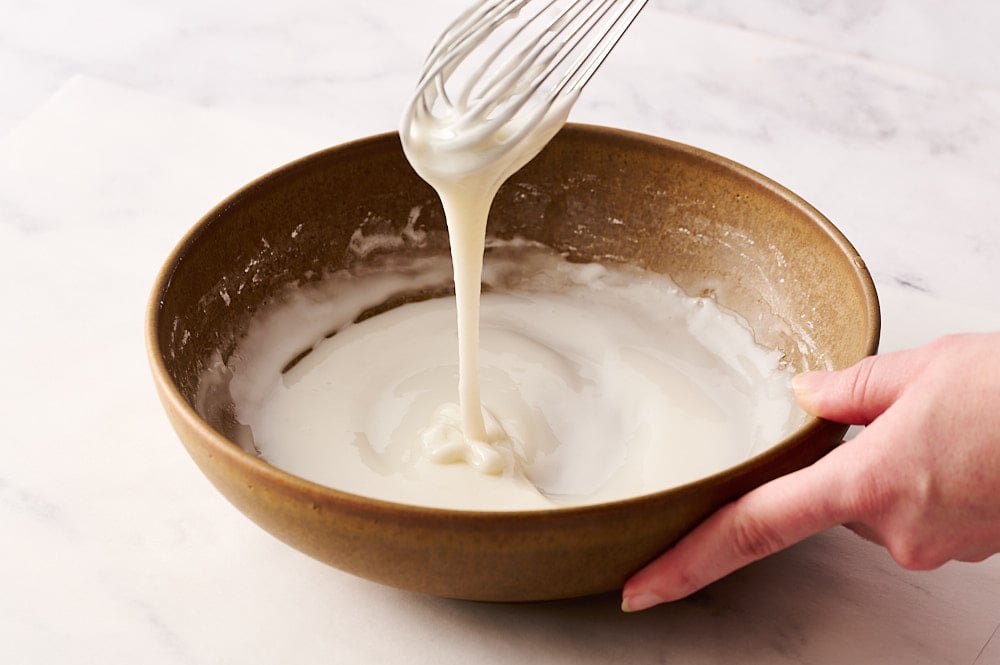 lemon poppyseed muffin icing in bowl with a whisk to show thick consistency