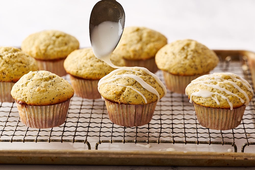 glazing lemon poppyseed muffins on a wire rack with a spoon