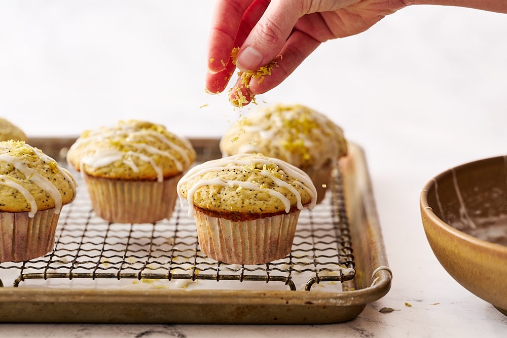 garnishing lemon poppyseed muffins with fresh lemon zest