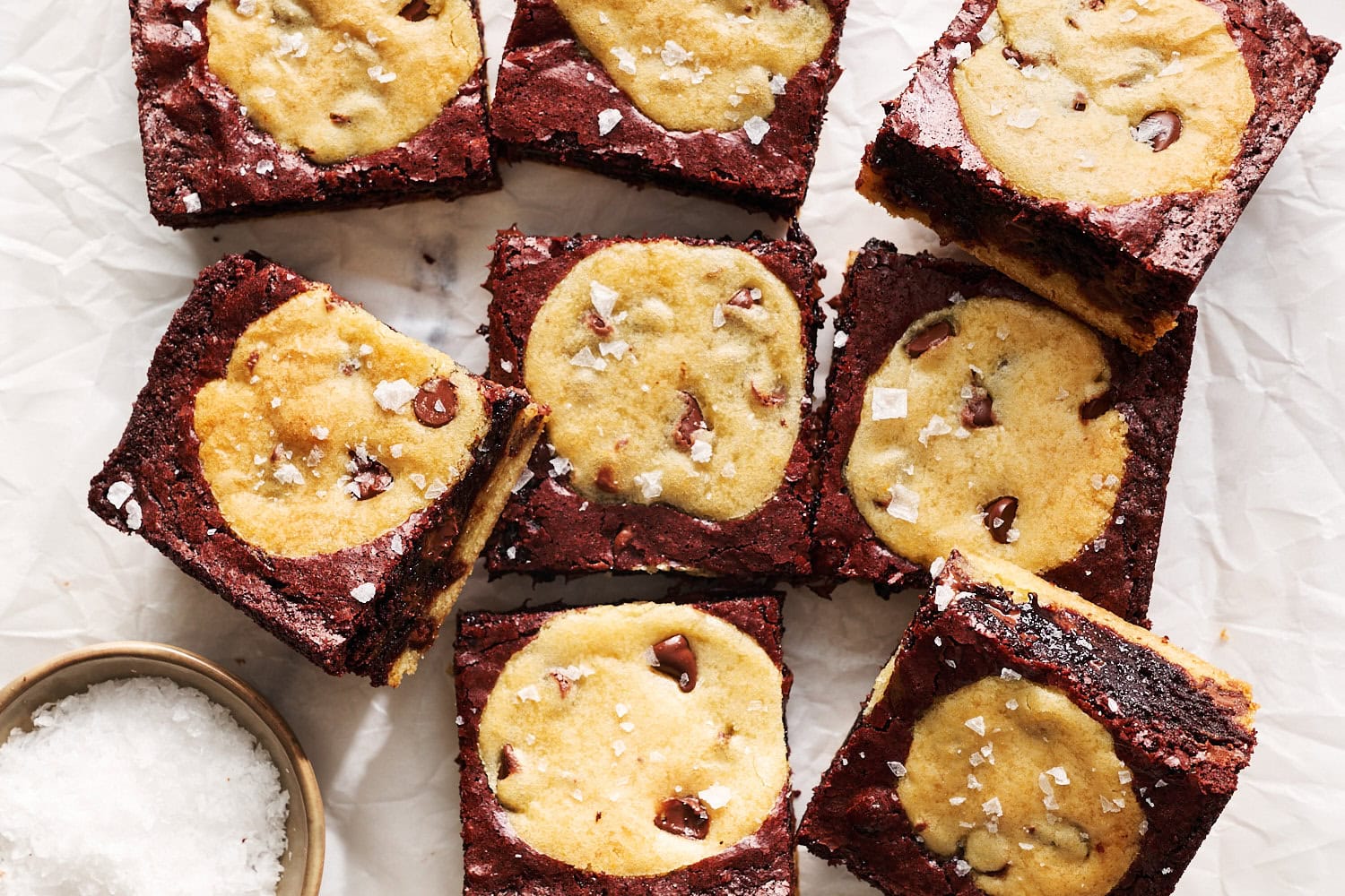 brookie squares on a white parchment sheet with a small bowl of flaky salt