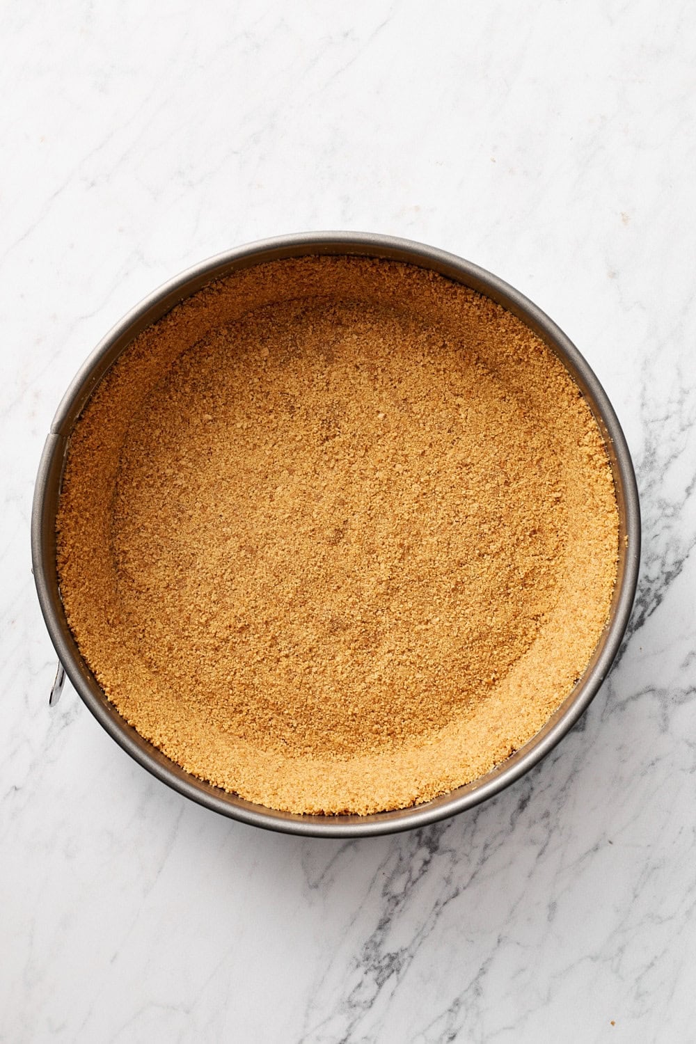 graham cracker crust pressed into a springform pan on a marble surface