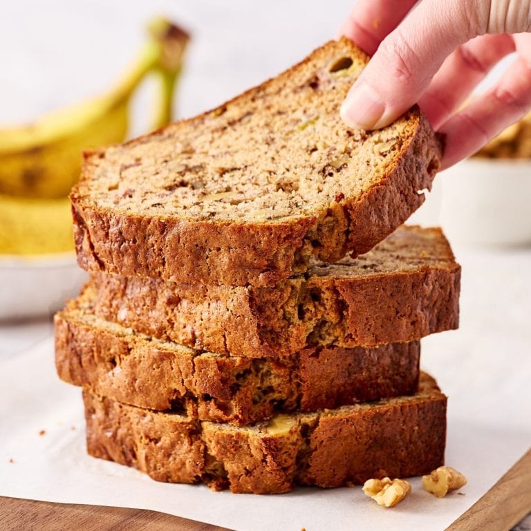 slices of banana bread stacked tall, with a hand removing the top to show its tender texture