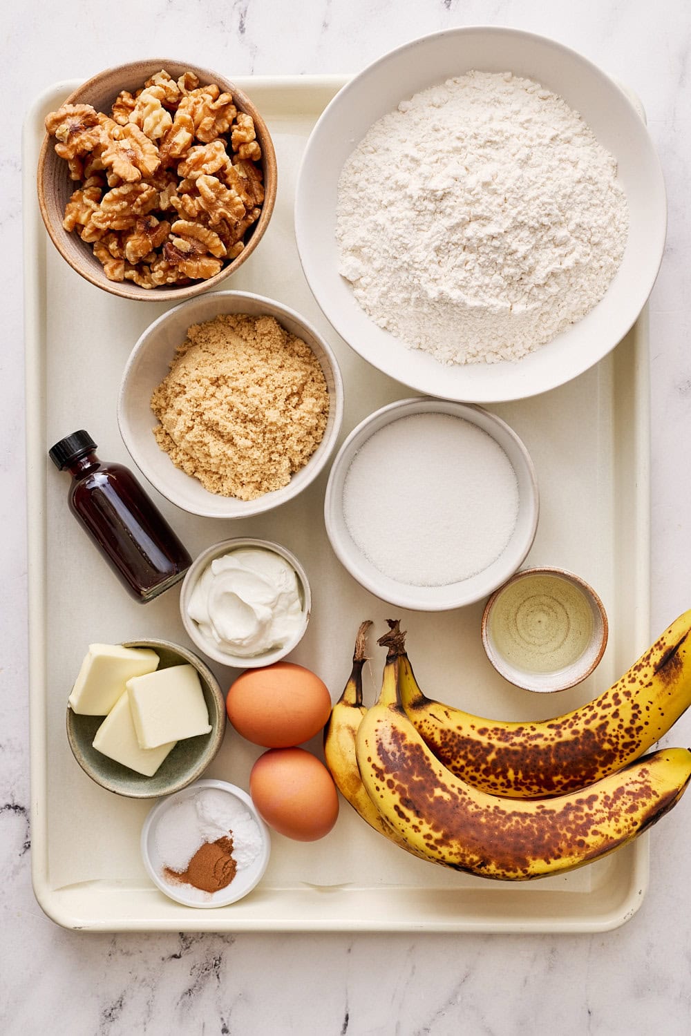 banana bread ingredients portioned out on a white rimmed baking tray