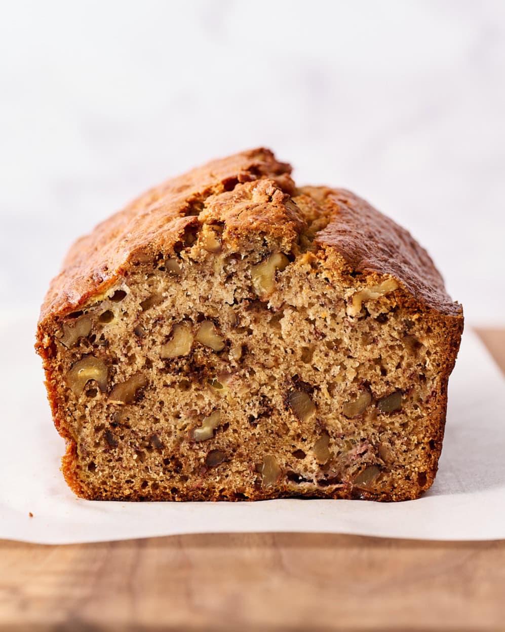 banana bread on a piece of parchment on a wooden board with one slice removed to reveal the tender interior