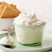 homemade marshmallow fluff in a glass container on a plate with a spoonful and a bowl of graham crackers in the background