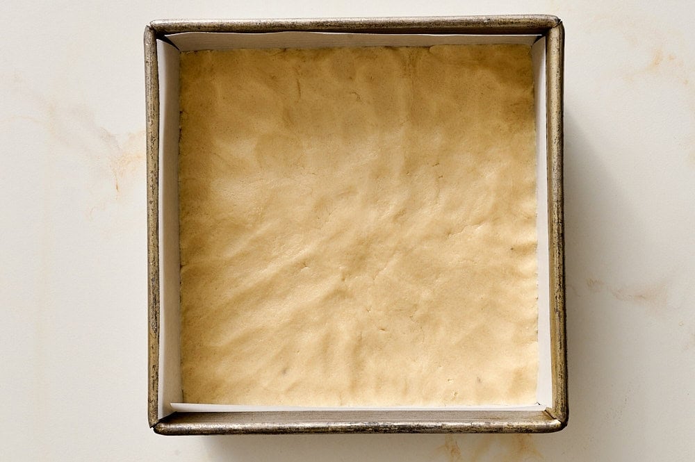 shortbread dough pressed into a square metal pan for strawberry cobbler bars
