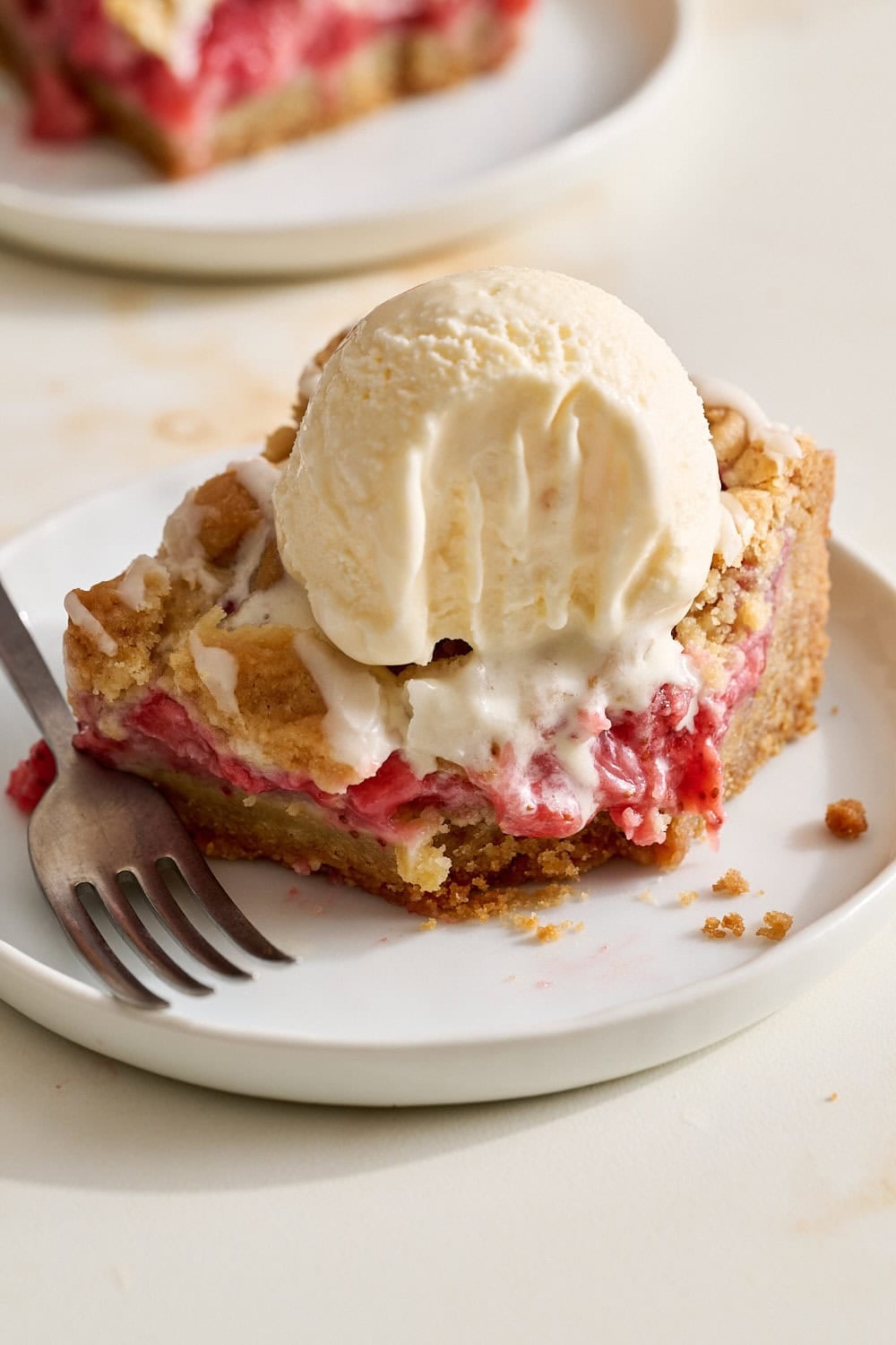 A strawberry cobbler bar on a small bite with a scoop of ice cream on top and a bite taken out