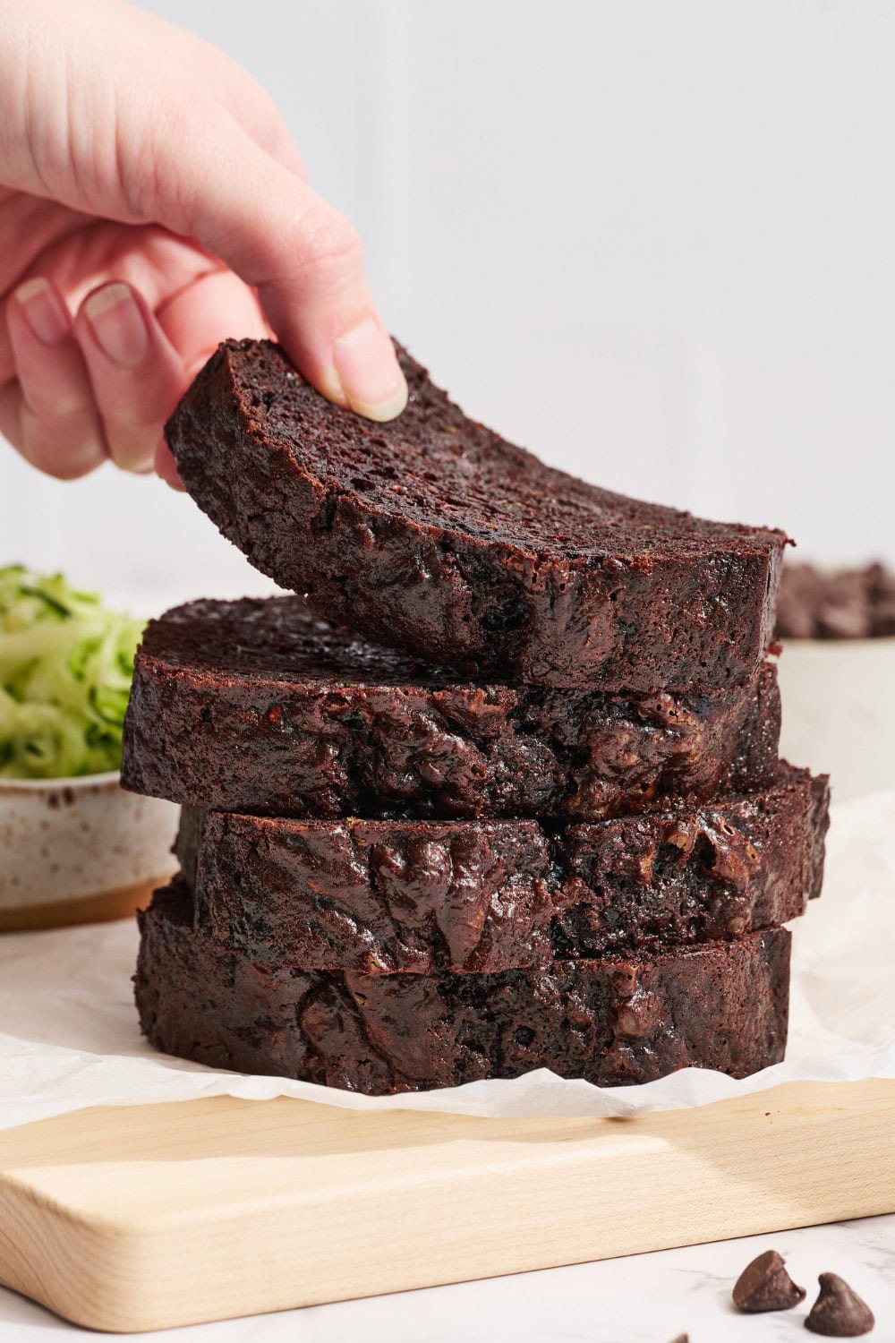 someone grabbing a slice of chocolate zucchini bread from a pile of slices
