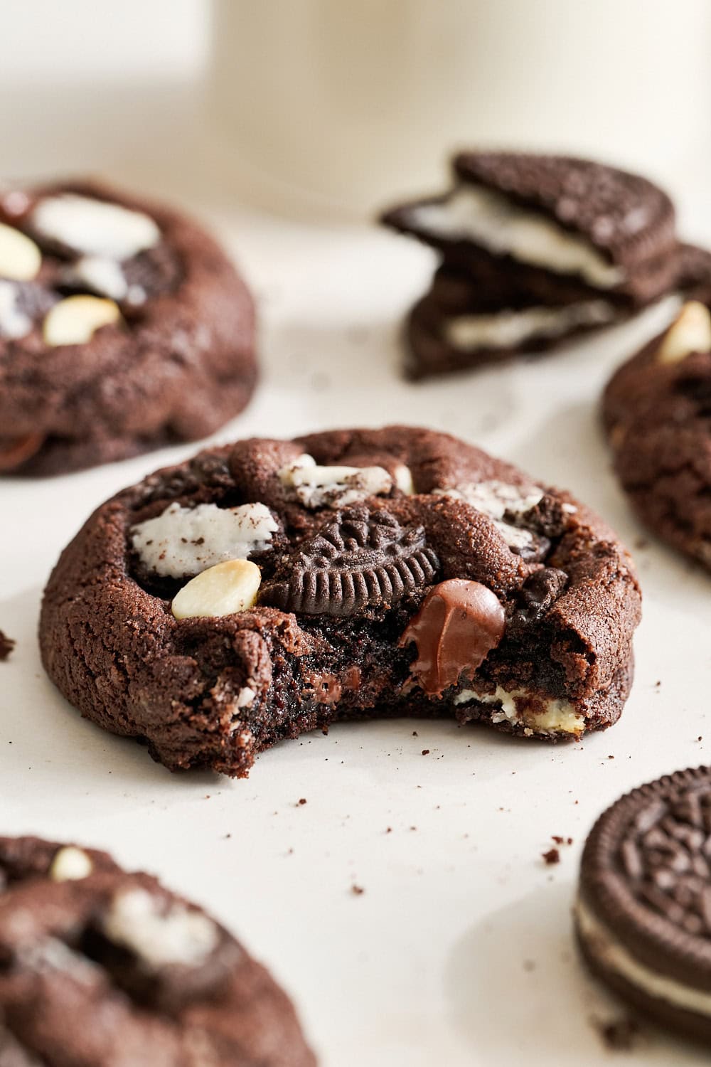 chocolate cookies & cream cookie with a bite taken out to show thick and fudgy interior, with Oreos and a glass of milk in the background