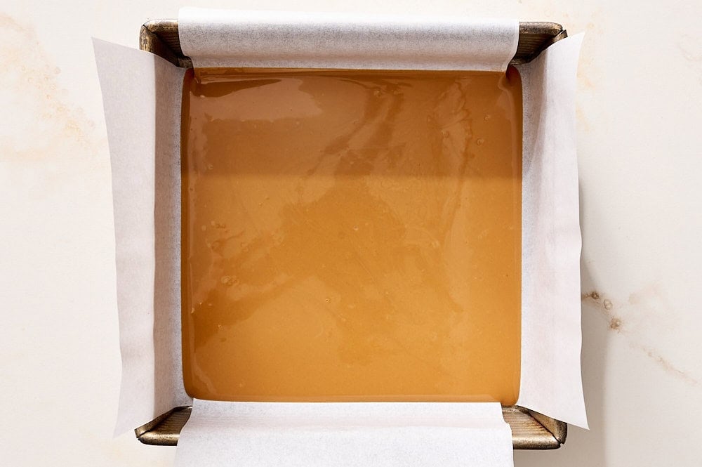 melted biscoff spread in a parchment lined square baking tray, ready to be frozen