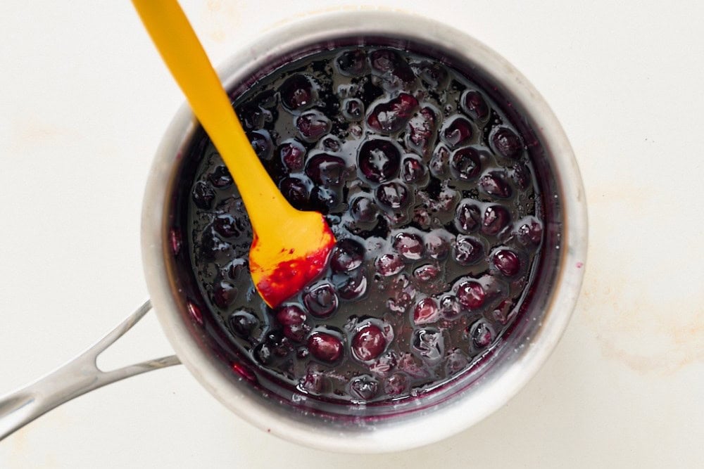 Blueberry sauce simmering in a saucepan with whole blueberries and a thick texture