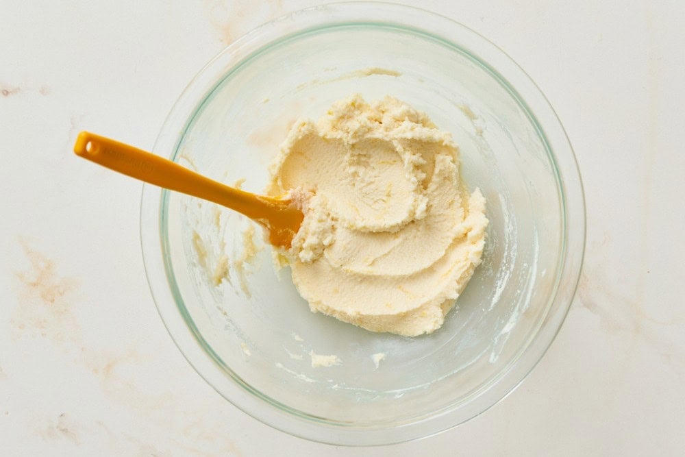 Thick mascarpone mixture with lemon zest and powdered sugar being mixed in a bowl