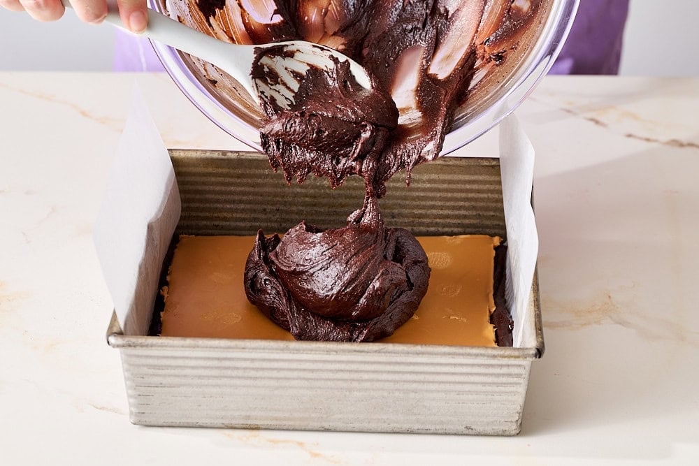 spooning remaining brownie batter over Biscoff spread in brownie pan