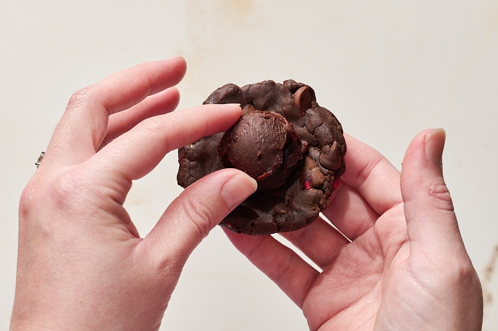 two hands holding a flattened piece of cookie dough, stuffing a ball of ganache into the center