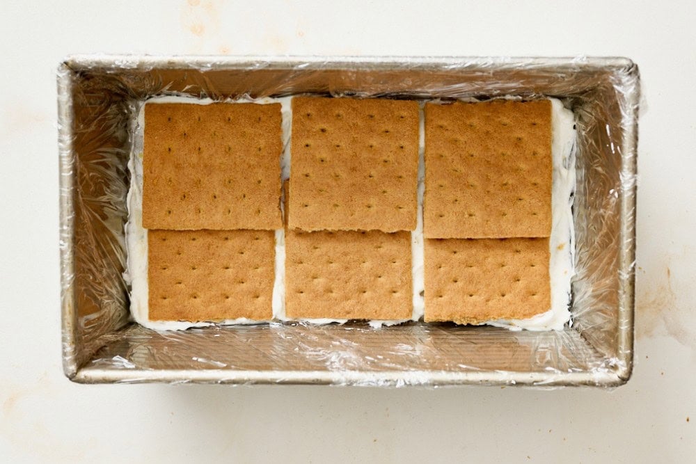 Loaf pan lined with whipping cream filling and a layer of graham crackers