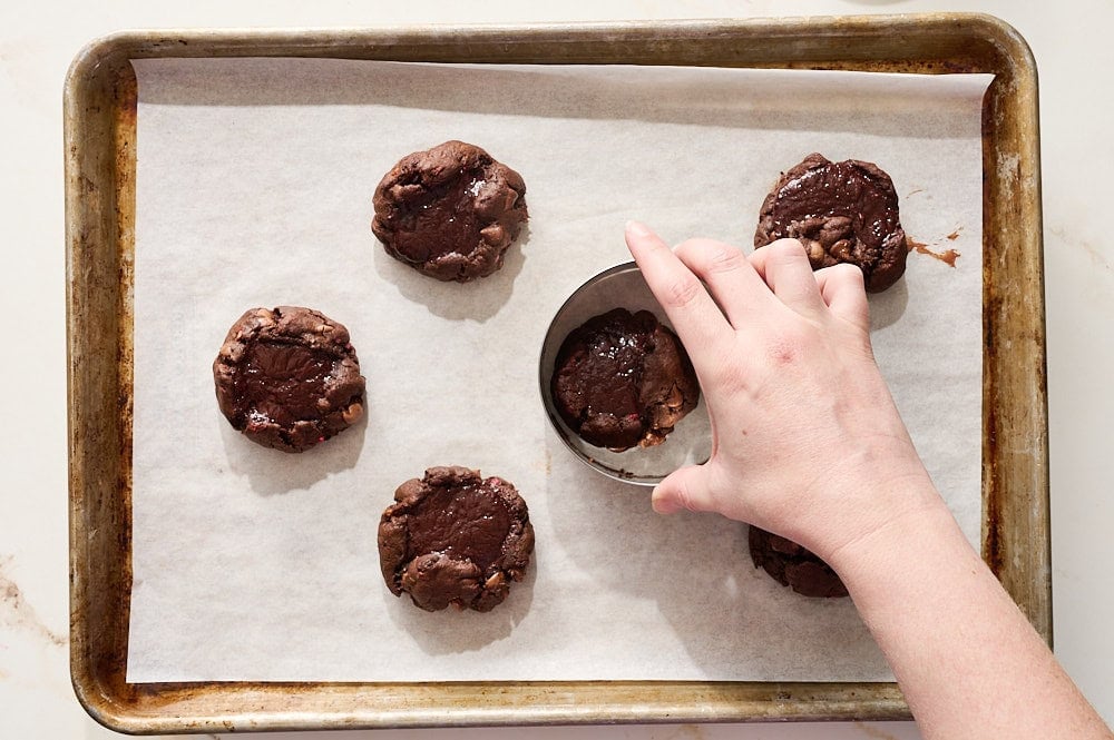 freshly baked raspberry chocolate cookies getting reshaped into perfect circles with a round cookie cutter