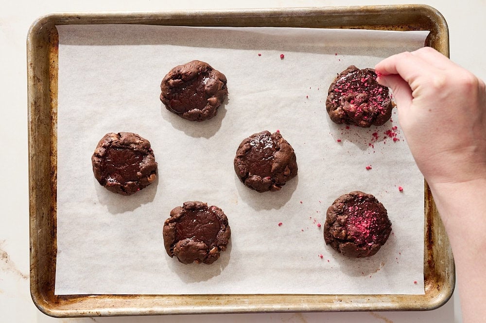 a hand sprinkling baked cookies with crushed freeze dried raspberries