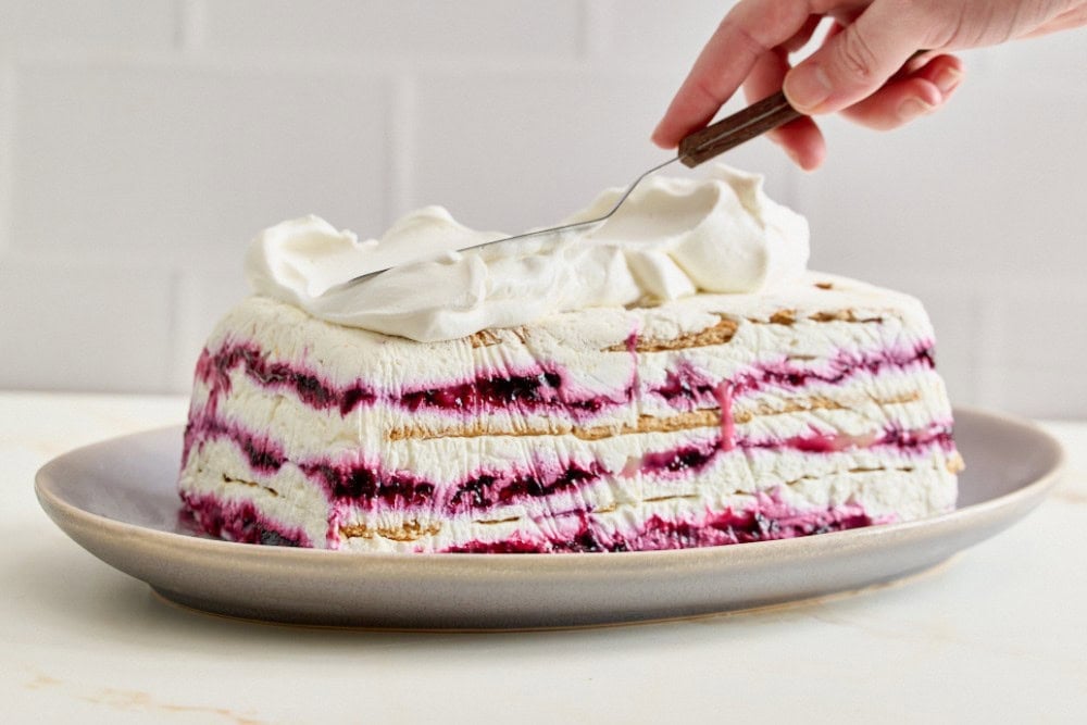 Blueberry lemon icebox cake being covered with whipped cream