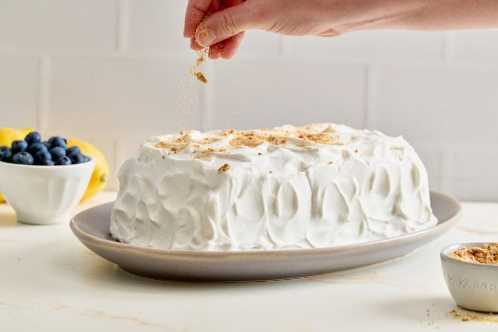 Fully coated blueberry lemon icebox cake being topped with crushed graham crackers