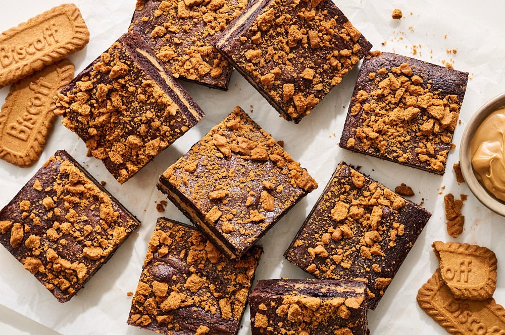 overhead of many Biscoff brownies on a piece of parchment paper, with extra Biscoff cookies and spread