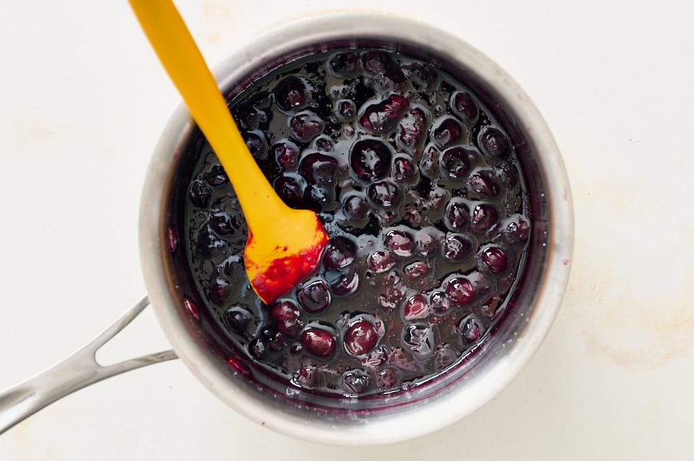 blueberry sauce cooking in a small saucepan, becoming thicker with saucier