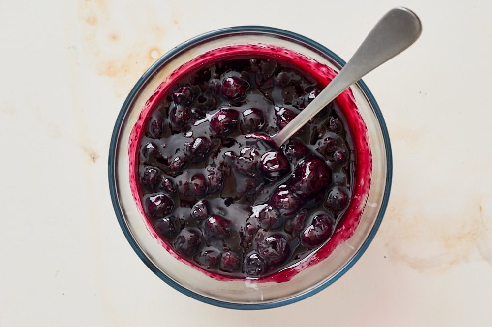 overhead of blueberry sauce in a glass bowl with a spoon