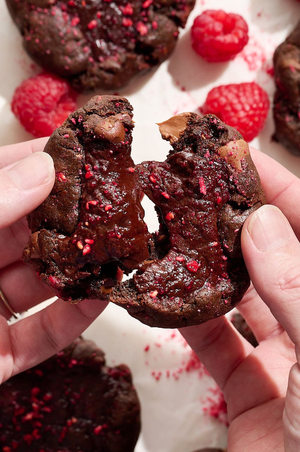 two hands splitting a raspberry chocolate cookie in half, showing the fudgy interior