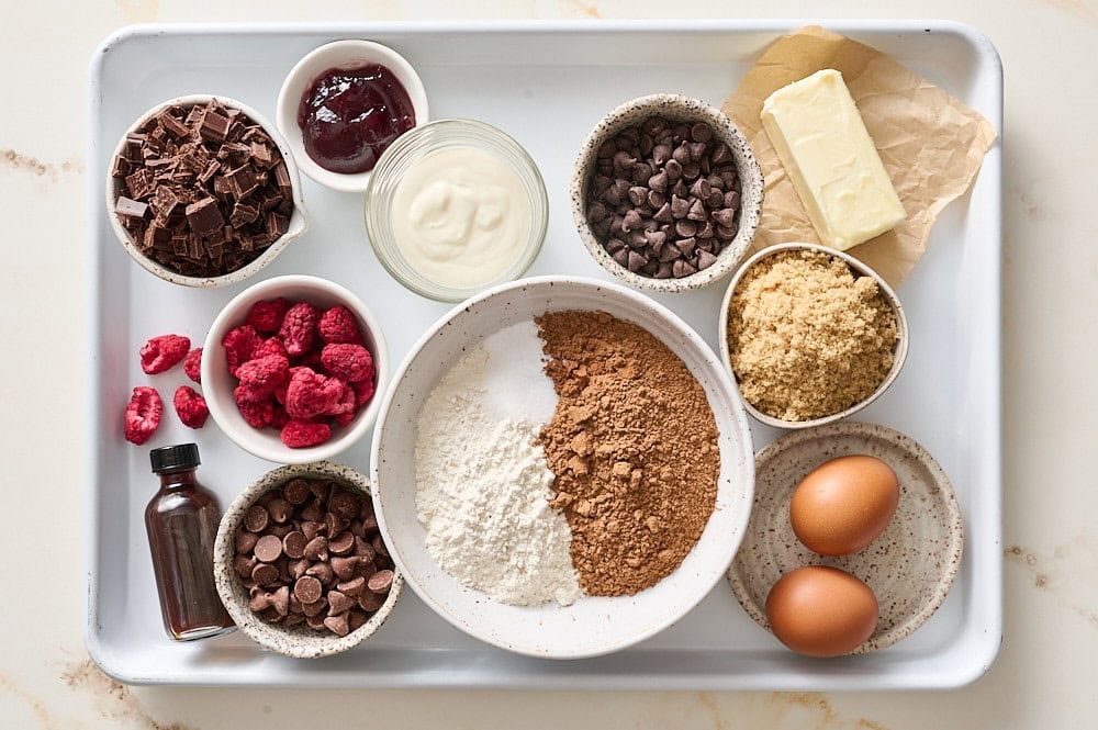 overhead view of all chocolate truffle raspberry cookie ingredients on a white rimmed baking sheet
