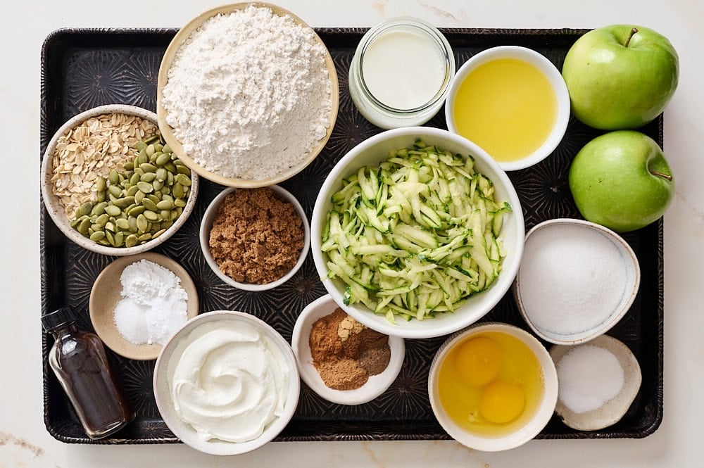 overhead view of all zucchini muffin ingredients portioned on a dark rimmed baking tray