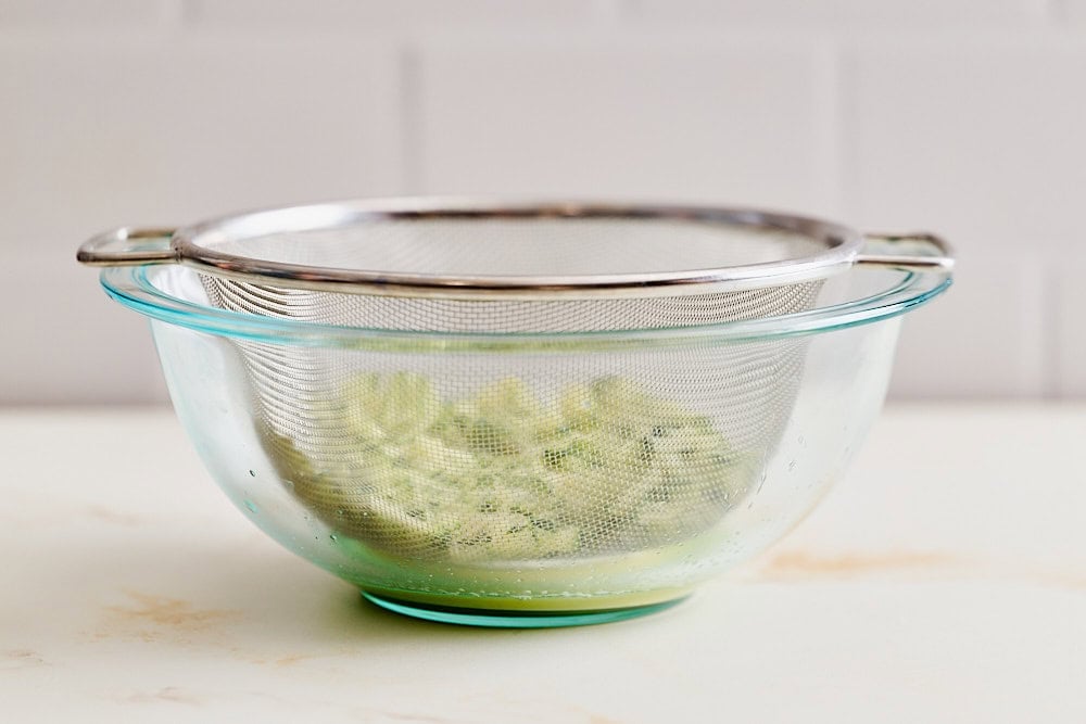 shredded zucchini and apple in a colander set over a glass bowl