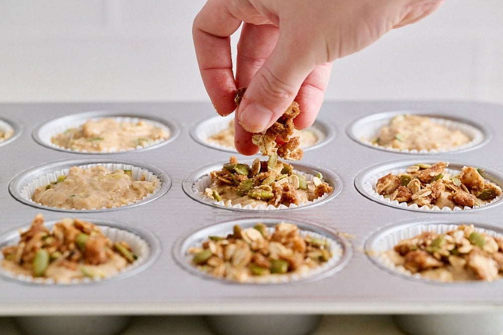 hand sprinkling crumble topping onto muffin batter inside pan
