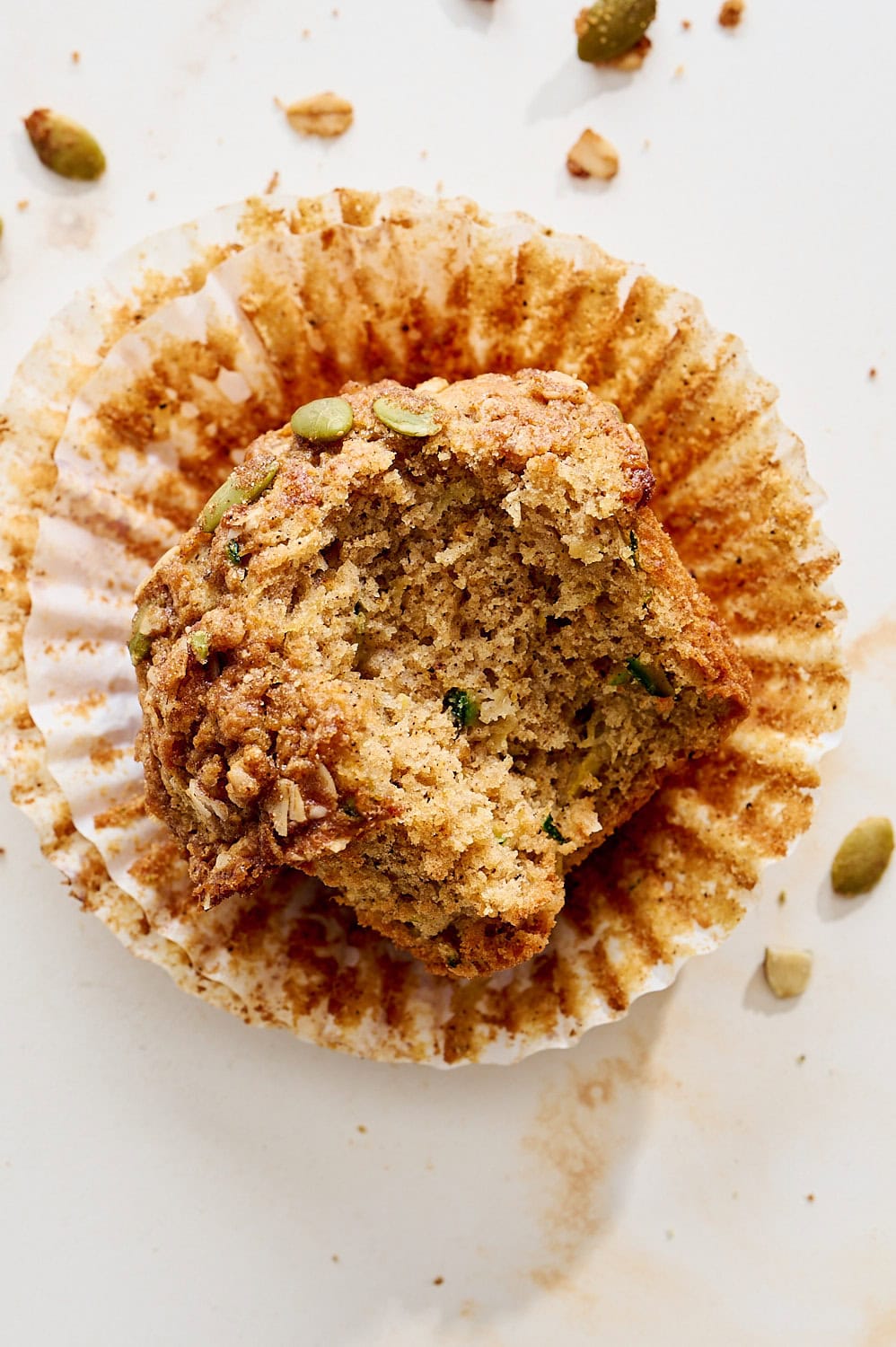 overhead view of a moist and fluffy zucchini apple muffin on its wrapper with a bite taken out