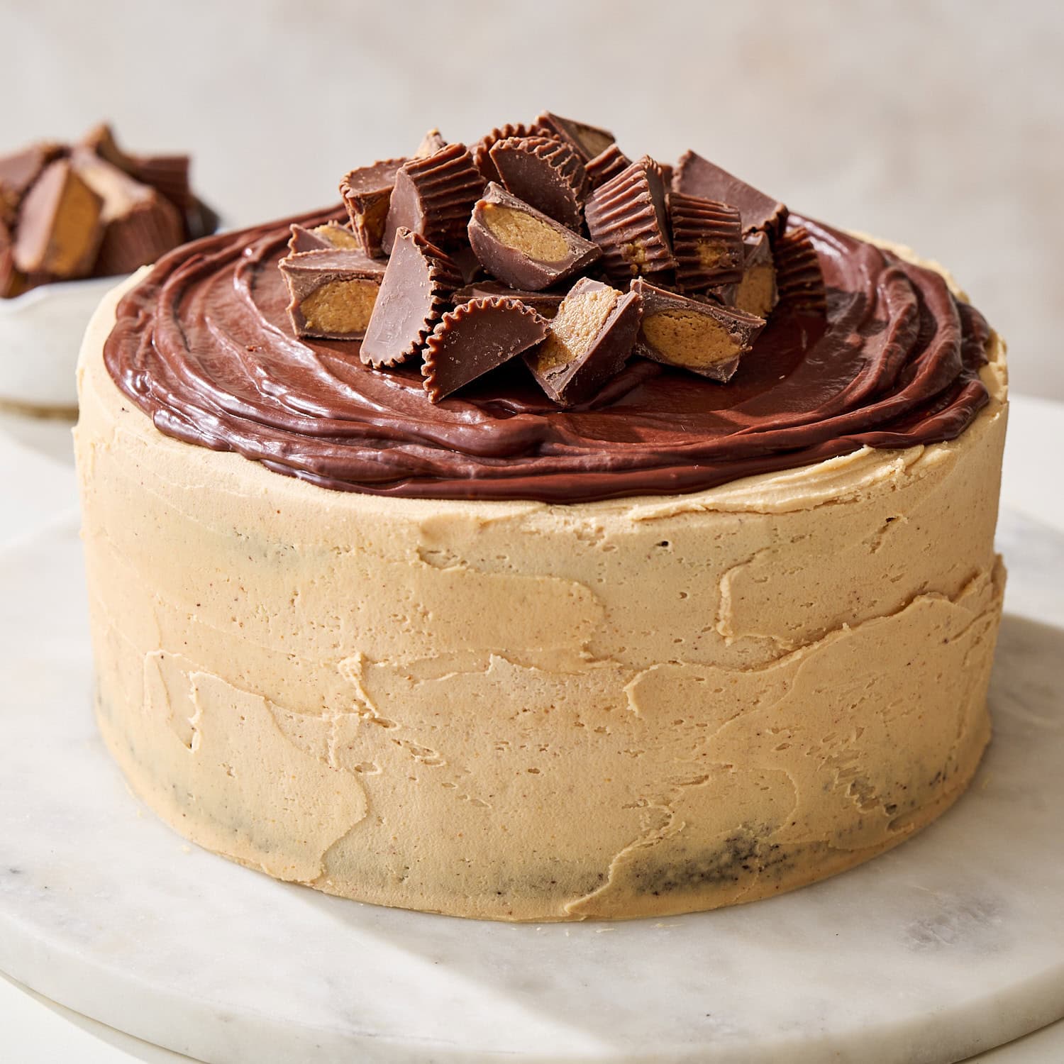frosted and decorated chocolate peanut butter cake on a marble cake round with peanut butter cups on top
