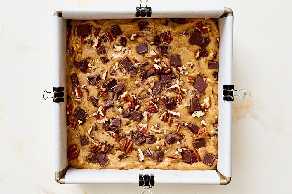 overhead view of unbaked bourbon pecan chocolate blondies in a square metal baking pan