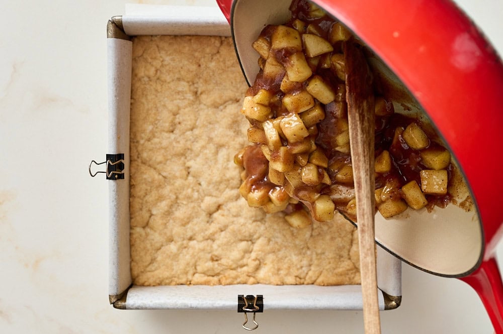 overhead view of pouring the apple pie filling over the par baked crust