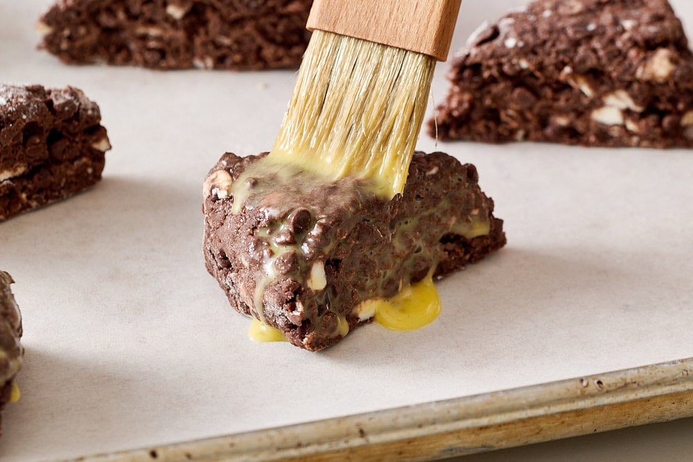 side view of a pastry brush applying egg wash to an unbaked scone