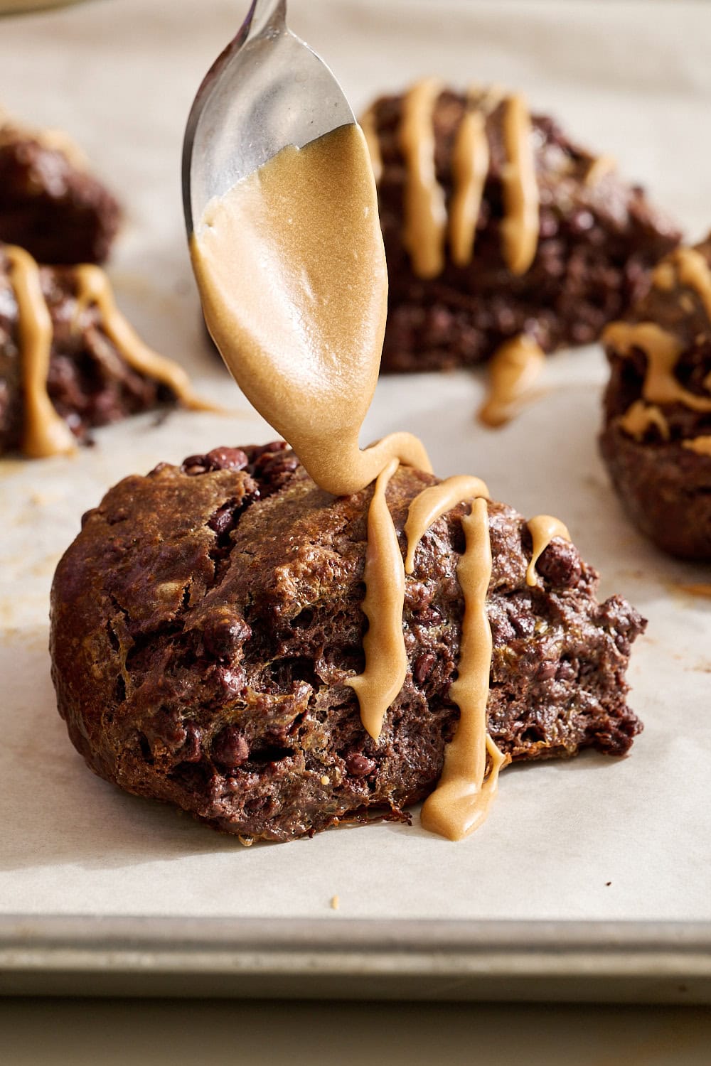 up close side view of a spoon drizzling espresso glaze on a mocha scone