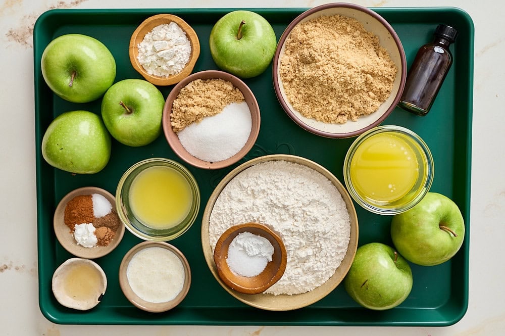 apple pie bar ingredients measured and organized on a dark green rimmed baking sheet