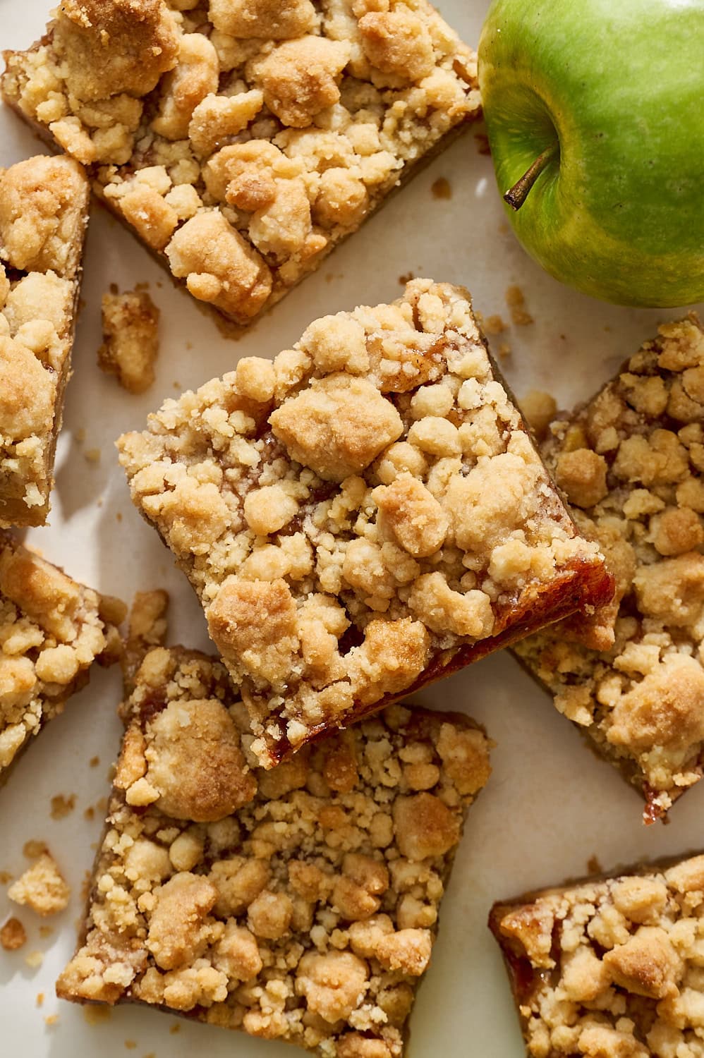 overhead view of several apple pie bars stacked on top of each other, with a granny smith apple in the corner