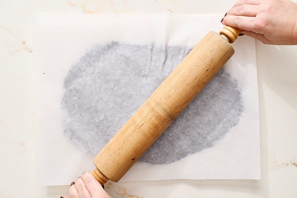 overhead view of black cocoa halloween cookie dough being rolled out between two parchment sheets