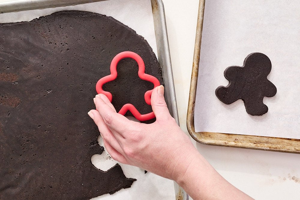 overhead view of black cocoa halloween cookie dough being cut into gingerbread shapes to make skeletons